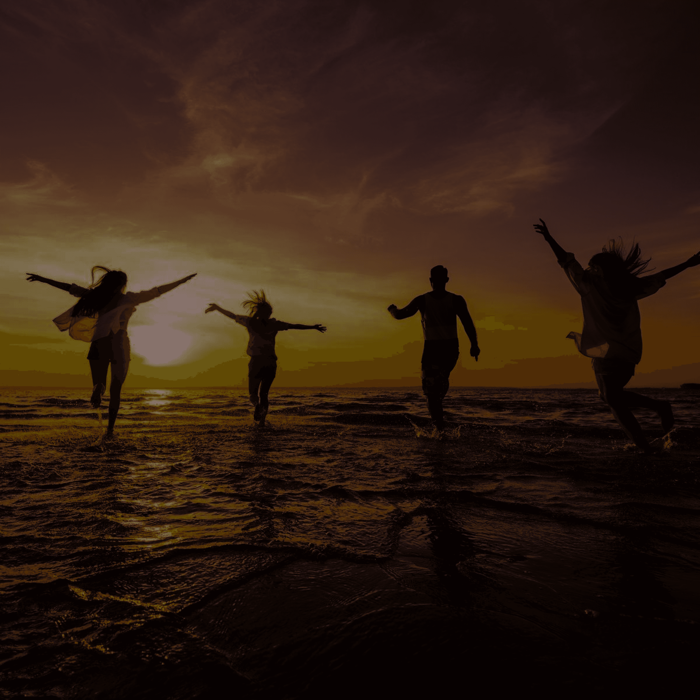 Friends running into the sea at sunset on holiday